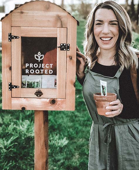 Whitney Sanger standing next to a Project Rooted sign holding a new plant.