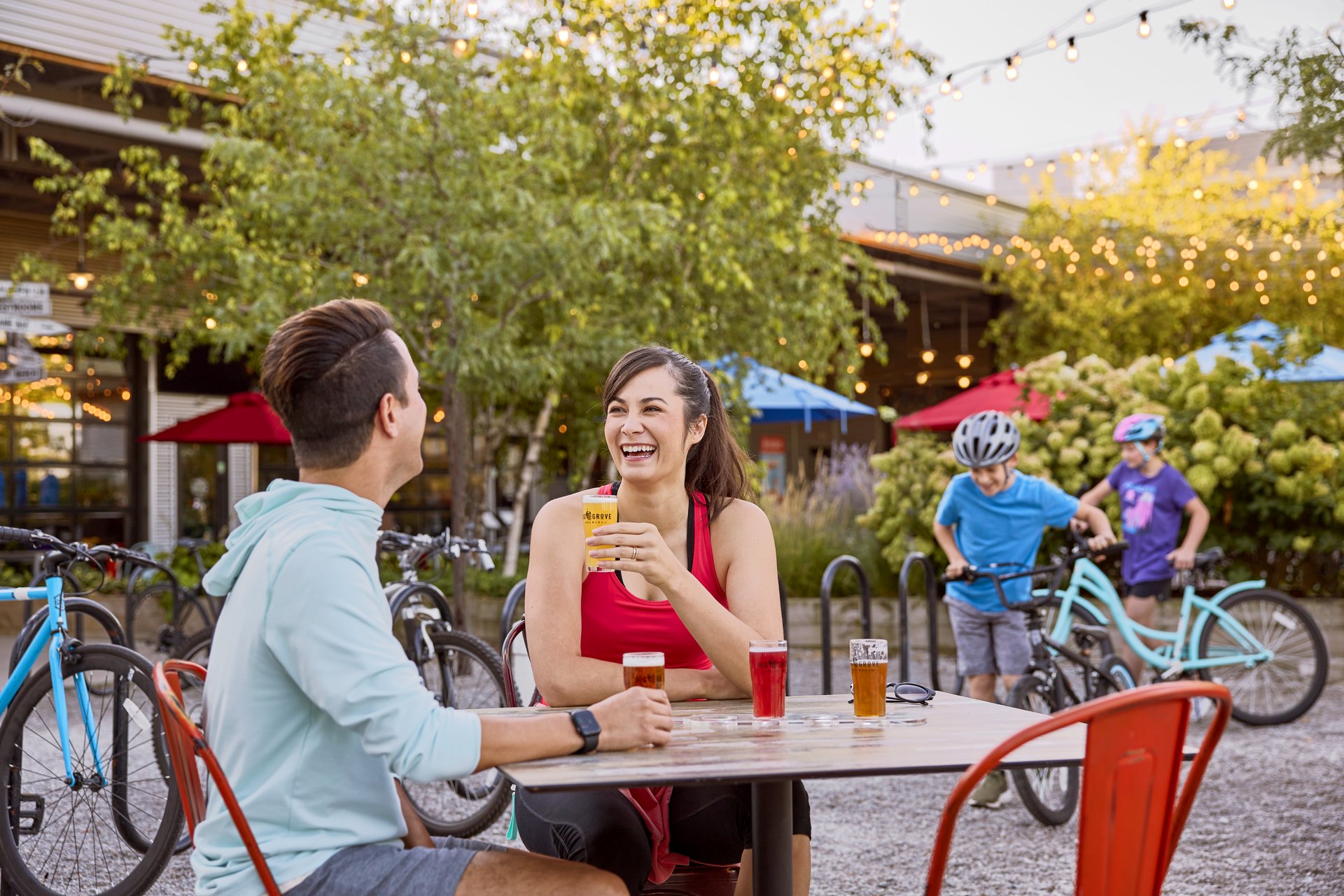 A man and a woman at a brewery with kids on bikes in the background