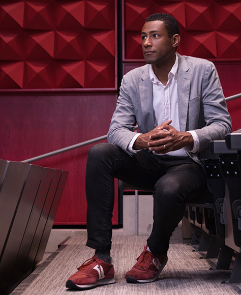 Man in suit sits in front of red wall