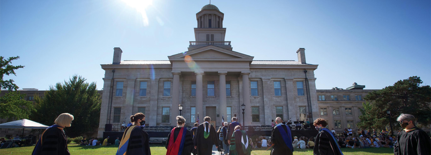 Group of graduates in their caps and gowns walking across campus.