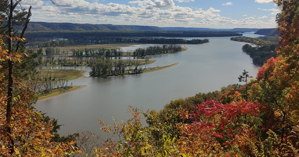 Red leaves frame a river scene cutting through the hilly landscape.