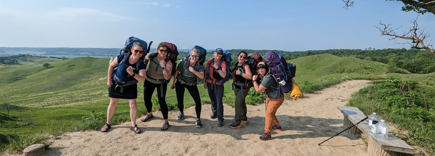 Group of women standing in a group with backpacks on.