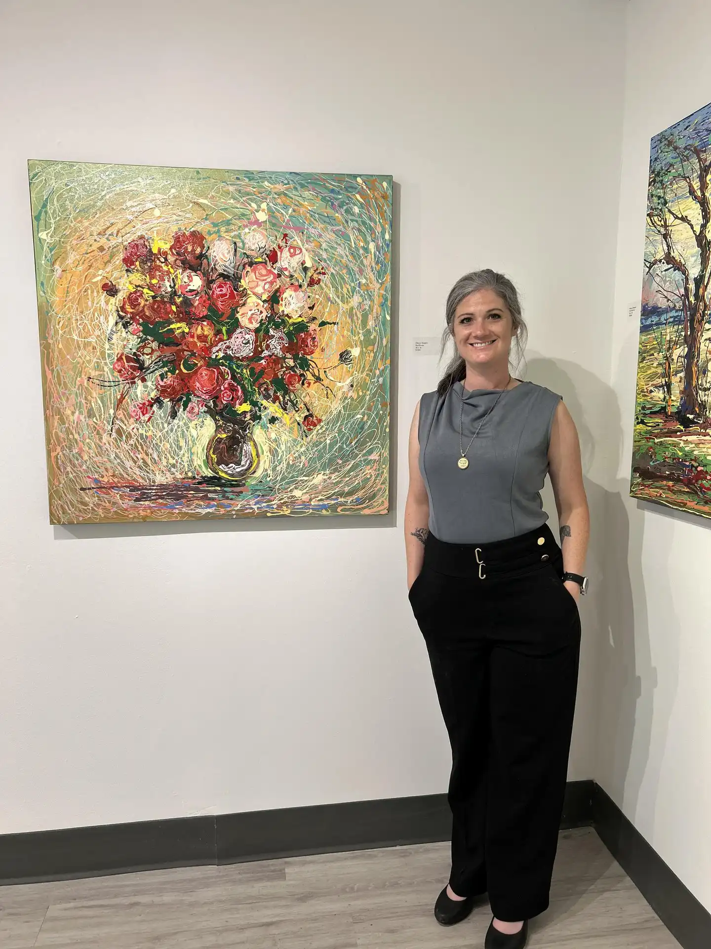 woman in a gray shirt standing next to a painting of flowers